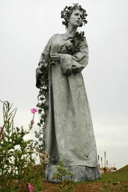 Living statue performers painted stone grey posing on plinths
